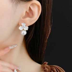 Close-up of white enamel flower earring with gold trim and pearl drop on model