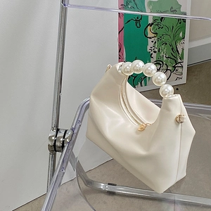 Detail of white PU leather bag featuring a pearl handle and gold zipper on a clear chair