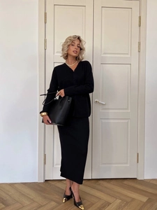 Chic black two-piece knit set with V-neck cardigan and skirt shown in a bright interior