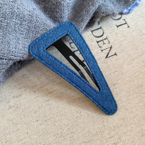 Dettaglio di un fermaglio per capelli triangolare in denim blu con cuciture e base in metallo