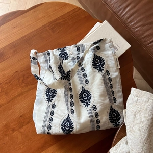 Détail de la broderie ethnique noire sur un sac en lin blanc avec étiquette de marque