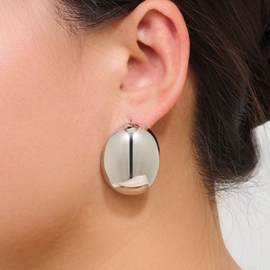 Close-up of polished silver oval stud earrings worn on ear showing reflective mirror finish