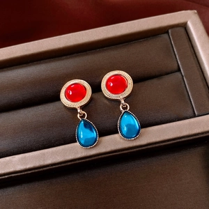Macro view of vintage gold earrings with red round stone and blue waterdrop resin pendant