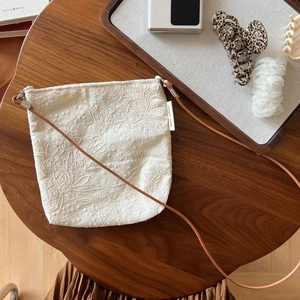 Detail of floral embroidery on beige linen phone bag with brown leather strap