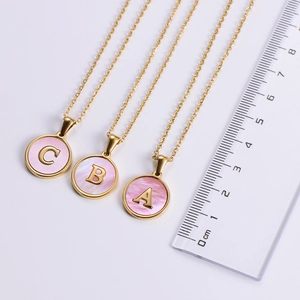 Close-up of golden letter pendants with pink shell inlay next to a measuring ruler