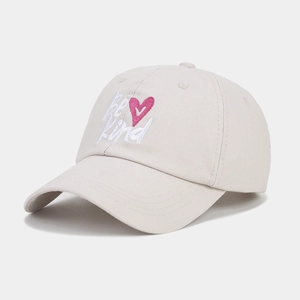 Gros plan de la broderie Be Kind et du cœur rose sur la casquette en coton beige