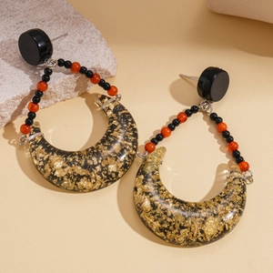 Detail of bohemian resin teardrop earrings with gold foil and bead accents on sand
