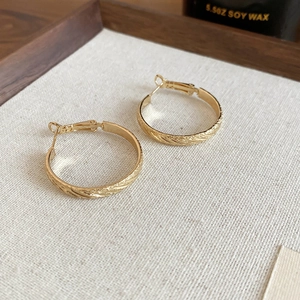Close-up of golden round hoop earrings with diagonal texture on minimalist fabric