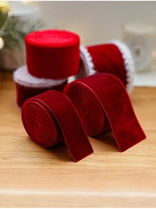 Close-up of red velvet Christmas ribbon with white stitched edges on a rustic wood surface