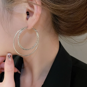Detailed close-up of tiered silver hoop earrings with textured inner ring and polished finish