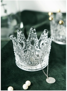 Detailed close-up of a crown-shaped clear glass jewelry holder on green velvet