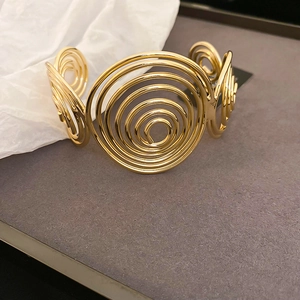 Macro detail of golden wave open cuff bracelet with concentric spiral geometric design