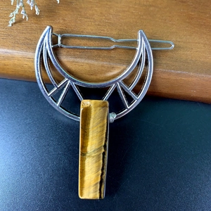 Close-up of silver crescent moon hair clip with tiger eye stone and hollow metal design