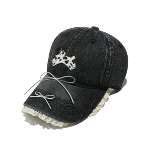 Détail d'une casquette en denim délavé avec broderie chiot, nœuds argentés et dentelle