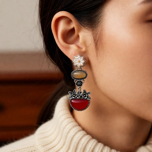 Detailed close-up of vintage flower earrings with red and yellow gemstones worn by model