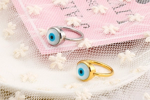 Macro view of gold and silver evil eye rings with blue enamel inlay on lace background