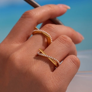Crossed golden ring with white pearls and pavé setting worn by model at the beach