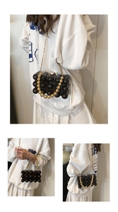 Detail of black spherical acrylic handbag with pearl handle and golden chain strap