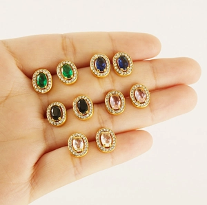 Close-up of five pairs of oval zircon earrings in green, blue, black, pink, and gold colors