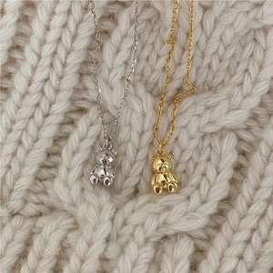 Detailed view of gold and silver bear pendants on fine chains over a white sweater