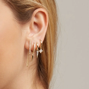 Detailed close-up of gold dangle earrings set with zircons and geometric studs on model