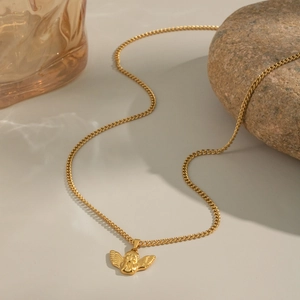 Collier avec pendentif ange en acier titane doré posé sur une surface en pierre neutre
