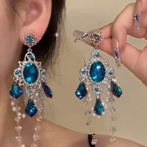 Detailed view of silver stud earrings with blue resin stones and dangling clear beads