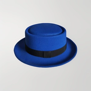 Royal blue pork pie hat with flat crown and black decorative band on gray background