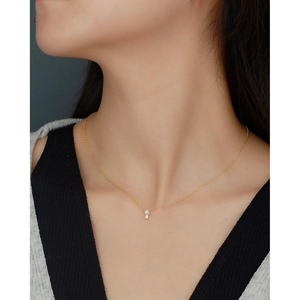 Close-up of a dainty gold necklace with a white pearl and sparkling zircon on a model