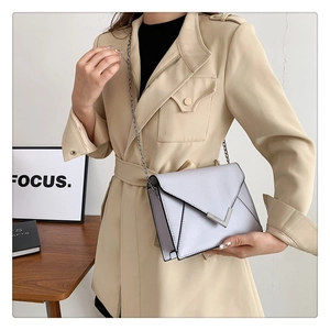 Detail of light grey chain shoulder bag with V-shaped metal trim on beige coat