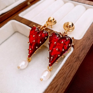 Close-up of vintage gold-plated heart earrings with red texture and baroque pearls