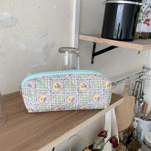 Detail of floral quilted pencil case with blue zipper on a wooden shelf in a natural setting