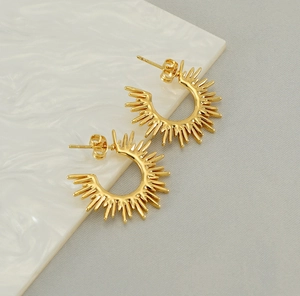 Close-up of golden sunburst fan-shaped earrings on a white marble and grey fabric surface