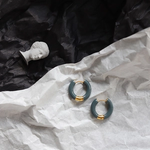 Detailed close-up of grey enamel and gold-plated circular hoop earrings on artistic base