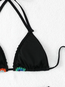 Close-up of black bikini top with colorful hand-woven ethnic beading on plush background
