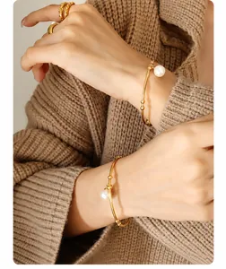 Detailed view of an open gold bangle with small beads and a round white pearl charm
