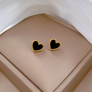 Close-up of heart-shaped gold stud earrings with black inlay on beige leather background