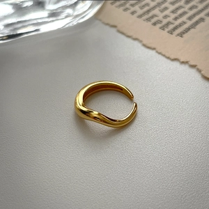 Macro detail of minimalist gold liquid-style irregular open ring on a textured surface