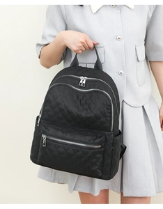 Detalle de mochila negra acolchada con cremalleras plateadas sostenida por una modelo