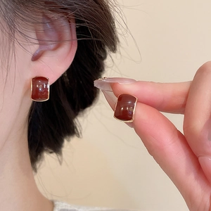 Detailed close-up of square red enamel earrings with gold frames worn by a model