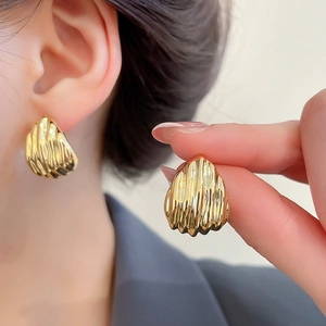 Macro detail of golden seashell earrings showing high-polish finish and ribbed texture