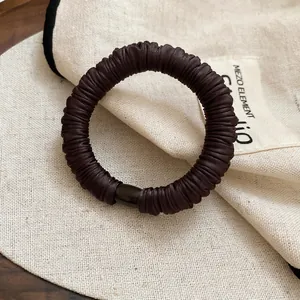 Minimalist dark brown pleated elastic hair tie with resin buckle on natural linen fabric