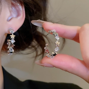Detailed view of silver C-shaped earrings with sparkling star cubic zirconia on ear