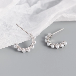 Detail of silver C-shape hoop earrings with white pearls on a minimalist background