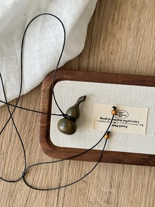Detail view of dark brown wooden gourd pendant on a black woven cord with wooden beads