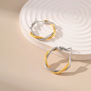 Minimalist twisted hoop earrings in gold and silver finish on a textured white base