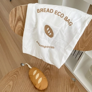 Foldable baguette shopping bag with bread plush pouch on a wooden chair