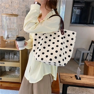 Polka dot canvas tote bag with brown leather handles held by a model in a cozy cafe setting