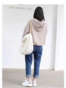 Back view of a person wearing a beige hoodie and large canvas shoulder bag in a studio