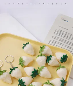 Detailed top view of realistic cream-colored PVC strawberry models and keychains on a yellow tray